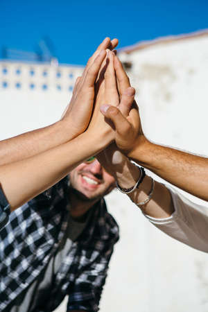 Crop faceless shot of friends giving high five on background of city in sunlight.の写真素材