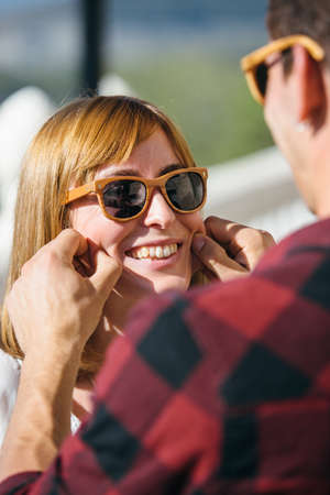 Young lovely couple in sunglasses having fun and male touching girl's cheeks.の写真素材