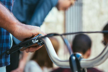 Close up crop shot of hand on bicycle handlebar on background of people talking.の写真素材
