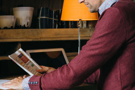 Crop young male in casual wear sitting and reading newspaper article at home.の写真素材