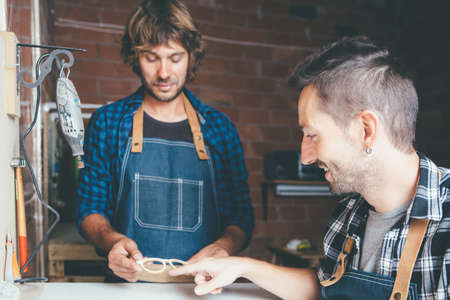 Two young craftsmen in working clothes making rim for glasses.の写真素材