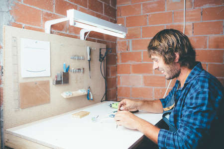 Young smiling artisan sitting at workplace and making rim for glasses.の写真素材