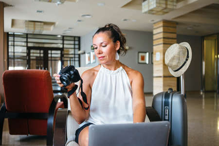 Female sitting with luggage and photo camera while using laptop.の写真素材