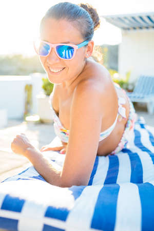 Smiling woman wearing sunglasses and lying in swimsuit on sunbed.の写真素材