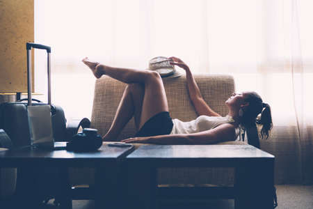 Side view of female resting on couch with luggage standing near.の写真素材