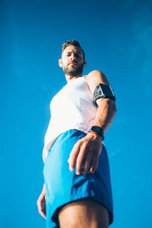 From below confident sportsman listening to music and looking at camera.