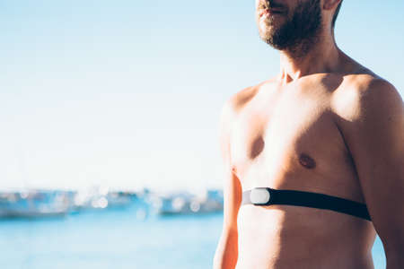 Shirtless fit man standing with heart rate monitor belt on his chest.の写真素材