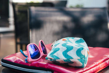 Horizontal outdoors shot of cosmetic case and blue sunglasses placed together.