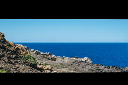 Horizontal outdoors shot of shoreline with rocks and calm blue sea.の写真素材