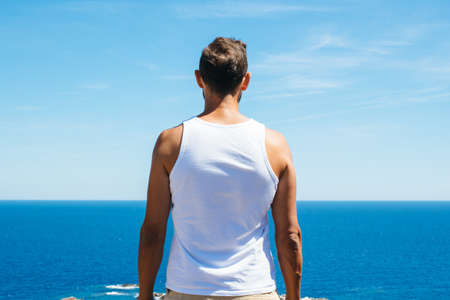 Back view of muscular man looking at calm sea horizon.