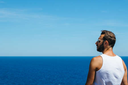 Back view of man looking away at blue peaceful ocean.の写真素材