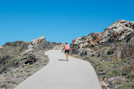 Back view of a woman with backpack taking walk on empty path in mountains.の写真素材