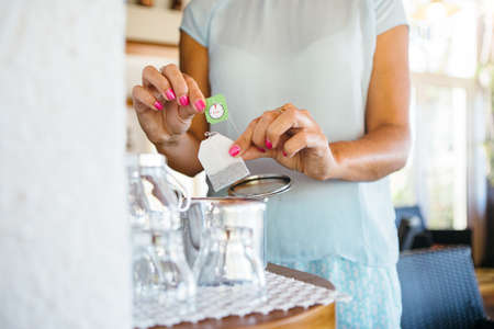 Unrecognizable woman putting the teabag to the cup making a cup of tea.の写真素材