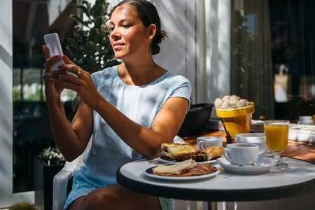 Smiling adult woman in cafebrowsing web and having breakfast.の写真素材