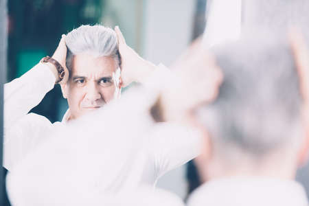 Back view of mature man holding head and touching haircut in barbershop.の写真素材
