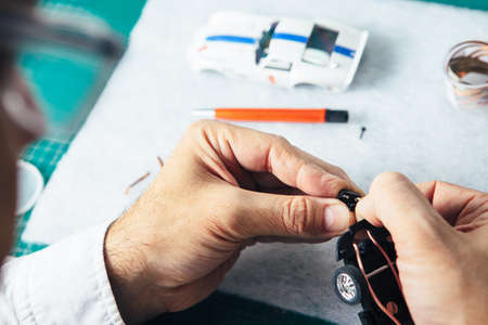 Horizontal close-up shot of master constructing miniature auto toy plugging a part.の写真素材