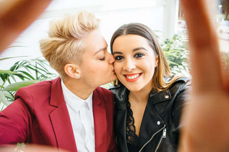Young lovely girl kissing girlfriend in cheek while both posing at camera.の写真素材