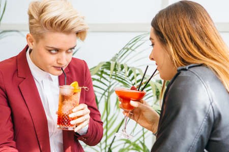 Beautiful girlfriends drinking cocktails while sitting at table in cafe and looking at each other.の写真素材