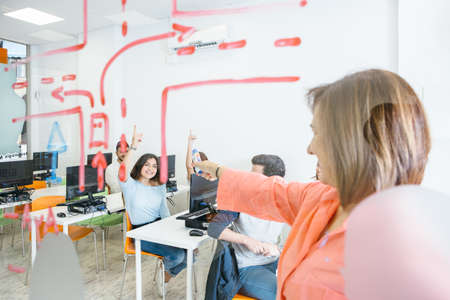 Mature woman asking questions while working with students in classroom.