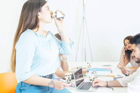 Pretty woman sitting on office desk and drinking during the meeting.の写真素材