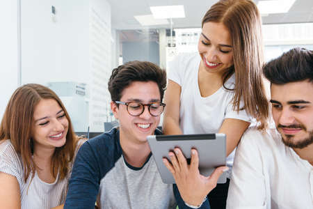 Cheerful men and women looking at tablet during brainstorm in office.