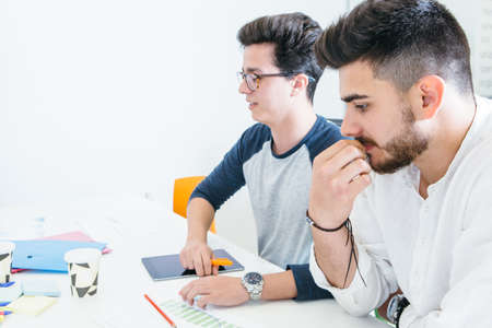 Two entrepreneurs men sitting at desk in office and brainstorming together.の写真素材