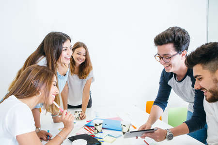 Cheerful young man showing digital tablet to coworkers at desk in office.