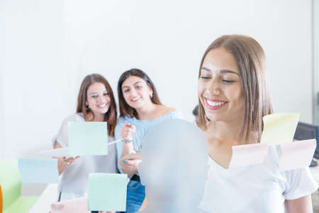 Young girl attaching stickers on wall of office with two cheerful coworkers on background.