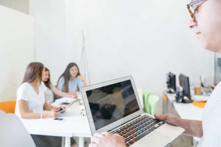 Side view of man in glasses using small laptop on background of students in classroom.の写真素材