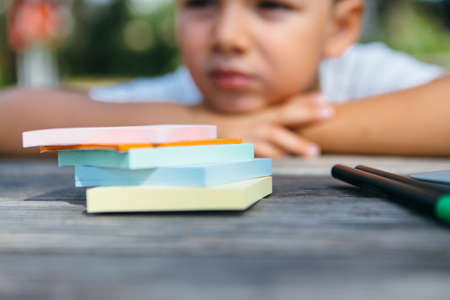 Close-up shot of stickers and pens on table with pensive boy on background in garden.の写真素材