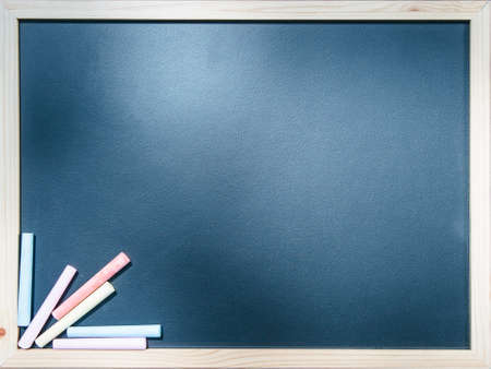 Close-up empty blackboard with different colorful chalk sticks.