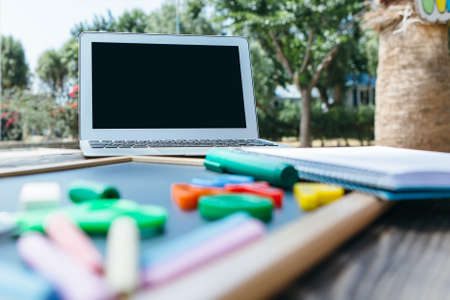 Empty laptop screen and colorful chalks on blackboard on table in park.の写真素材