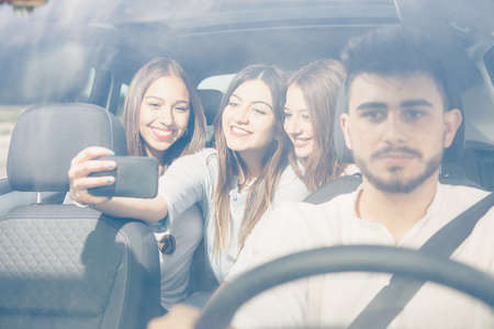 Group of friends making a selfie with a mobile phone sitting on the back of a car on a journeyの写真素材