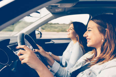 Side view of a girl driving a car with her girls friend beside herの写真素材