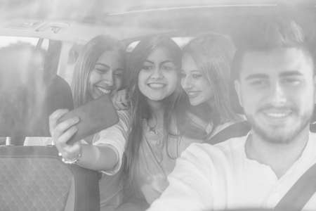 Group of girls friends making a selfie with a mobile phone sitting on the back of a car on a journey - Black and Whiteの写真素材