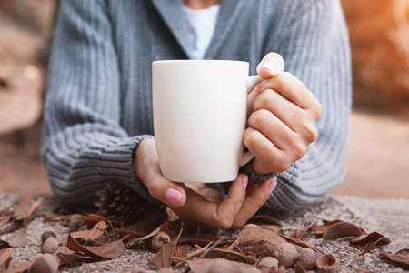 Close up of hands of a woman holding a cup of coffee on a autumn atmosphere. Copy space area availableの写真素材