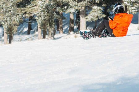 Young woman snowboarder is stopped with the snowboard removed on a snowy track while is using the mobile phone. Copy space area availableの写真素材