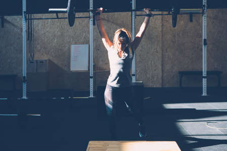 Young woman athlete doing jerks with barbell at box gym on a cross-fit routineの写真素材