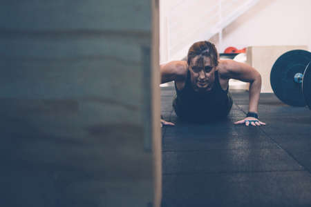 Close up of a young athlete woman doing burpees on a cross-fit workout at the box gym. Copy space...