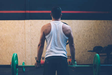 Back view of a young male athlete doing a deadlift exercise with a barbell on a cross fit routine at the box gymの写真素材
