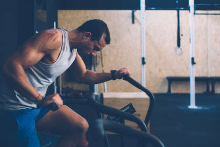 Side view of a young sporty man doing calorie assault exercise on a fitness routine at the box gym