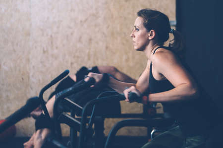 Side view of a young sporty woman doing calorie assault exercise with her colleague doing glute ham developer routine on a fitness routine at the box gymの写真素材