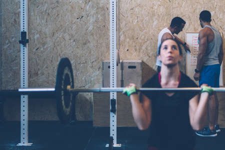 Two men checking workout day routine on a fitness workout at the box gym while woman does barbell exerciseの写真素材