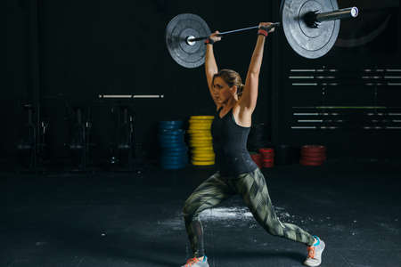 Young woman athlete does jerks with barbell at box gym on a fitness routine. Copy space area...