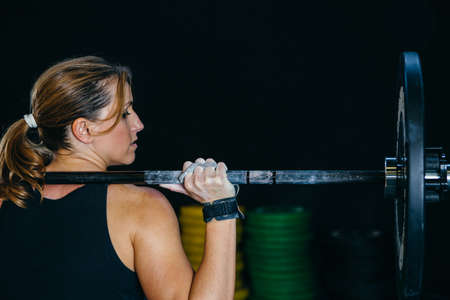 Back view of a young sporty woman doing back push press or military press exercise with a barbell over her shoulders on a fitness routine at the box gymの写真素材