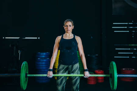Front view of a young female athlete doing a dead lift exercise with a barbell on a fitness routine at the box gymの写真素材