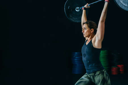 Young woman athlete does jerks with barbell at box gym on a fitness routine. Copy space area availableの写真素材