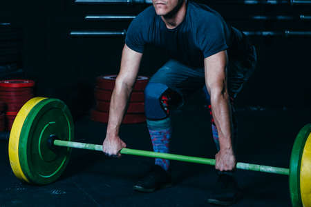 Cropped view of a concentrated young sporty man ready to do a barbell snatch exercise on a fitness...
