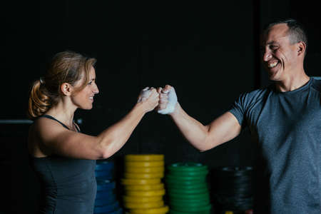 Smiling sporty young woman and man hitting fists on a fitness routine at the box gymの写真素材