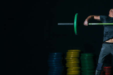 Close up of a cropped view of a young sporty man doing power snatch with barbell on a fitness routine at the box gym. Copy space area availableの写真素材